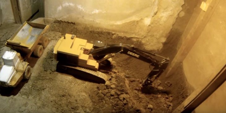 Мужчина 14 лет строит подвал игрушечными экскаваторами на пульте управления