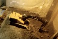 Мужчина 14 лет строит подвал игрушечными экскаваторами на пульте управления